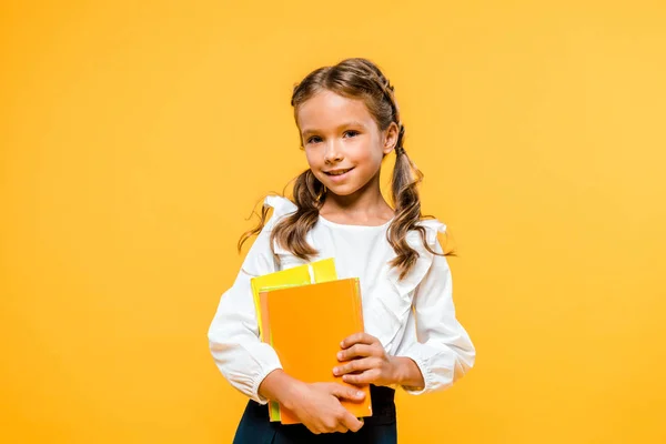 Niño feliz sosteniendo libros y sonriendo aislado en naranja - foto de stock