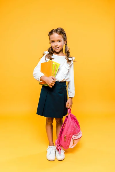 Niedliches und glückliches Kind mit Büchern und Rucksack auf orange — Stockfoto