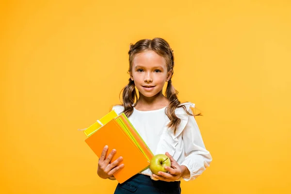 Happy kid holding books and tasty apple isolated on orange — Stock Photo