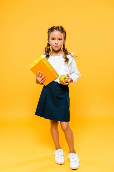 Bambino felice che tiene libri e mela gustosa mentre in piedi su arancione — Foto stock