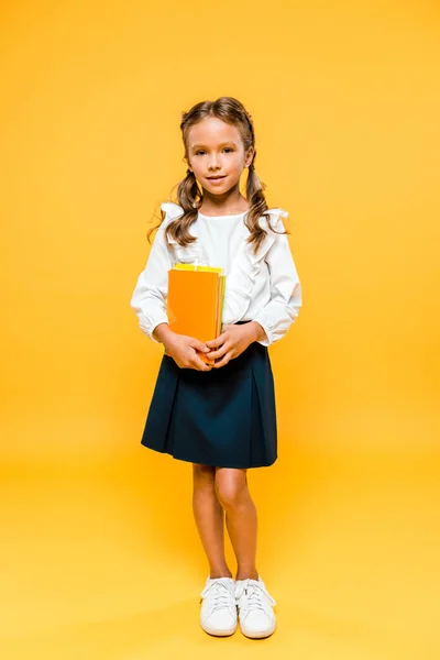 Smiling and cute kid holding books and standing on orange — Stock Photo