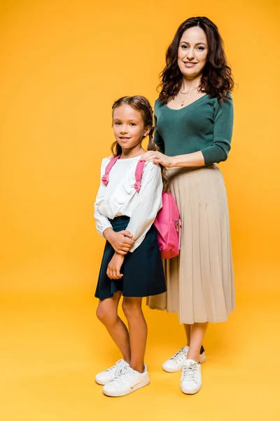 Glückliche Mutter steht mit fröhlichem Schulmädchen auf Orange — Stockfoto