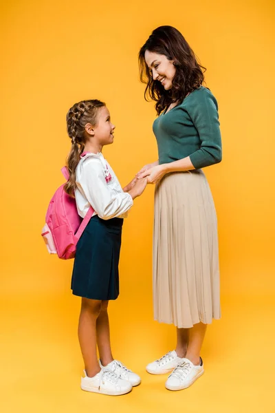 Happy mother holding hands with cheerful schoolgirl on orange — Stock Photo