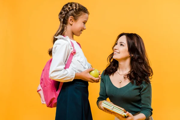 Happy mother holding books near daughter with apple isolated on orange — Stock Photo