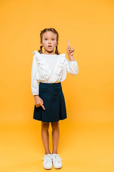 Surprised schoolkid pointing with fingers while standing on orange — Stock Photo