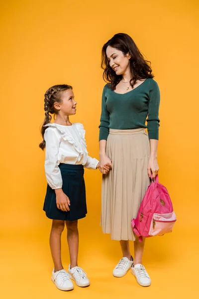 Attractive mother holding hands with cute schoolgirl on orange — Stock Photo