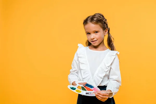 Glückliches Schulmädchen mit Palette und Pinsel isoliert auf orange — Stockfoto