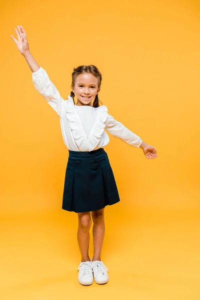 Fröhliches Schulmädchen, das mit den Händen über dem Kopf auf orange steht — Stockfoto