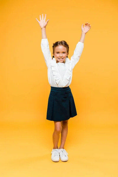 Glückliches Schulmädchen, das mit Händen über dem Kopf auf orange steht — Stockfoto