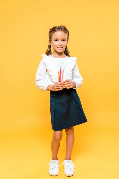 Heureux écolier tenant crayons de couleur sur orange — Photo de stock