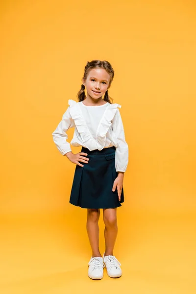 Heureux écolier debout avec la main sur la hanche sur orange — Photo de stock