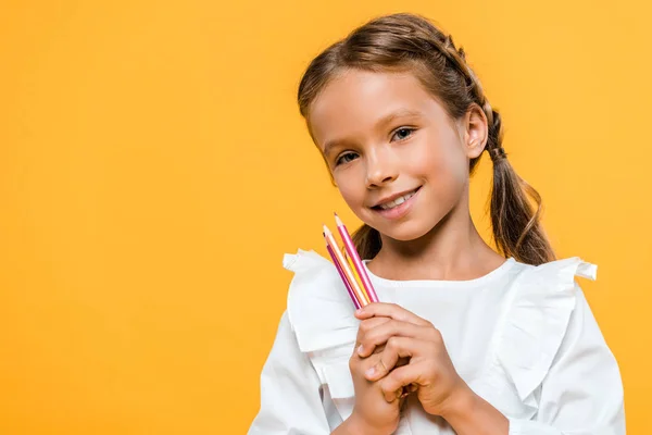 Cheerful schoolgirl holding color pencils isolated on orange — Stock Photo