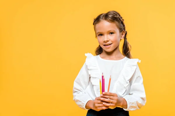 Colegial positivo sosteniendo lápices de color aislados en naranja - foto de stock