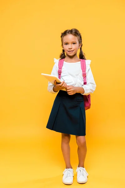 Cheerful schoolchild with pink backpack holding book on orange — Stock Photo