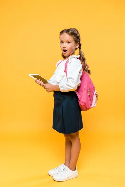 Sorprendido colegial sosteniendo tableta digital con pantalla en blanco en naranja - foto de stock