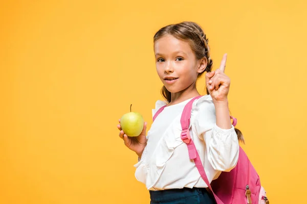 Adorable schoolkid holding apple and pointing with finger isolated on orange — Stock Photo
