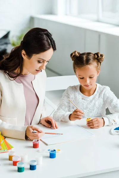 Attractive mother ad cute daughter holding paintbrushes — Stock Photo