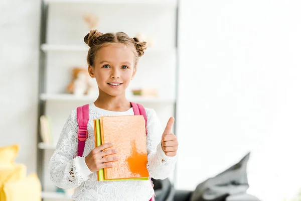 Happy schoolgirl holding books and showing thumb up at home — Stock Photo