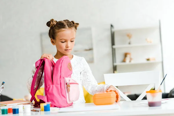 Мила школярка тримає обідню коробку біля рожевого рюкзака — стокове фото
