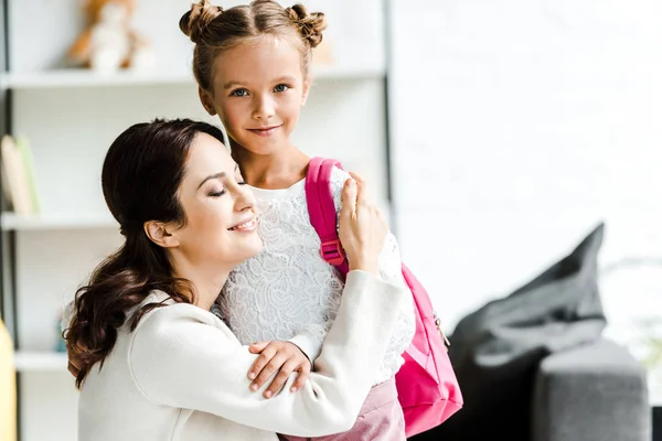 Mãe feliz abraçando filha alegre com mochila em casa — Fotografia de Stock