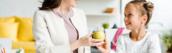 Tiro panorámico de madre feliz dando manzana a la hija - foto de stock