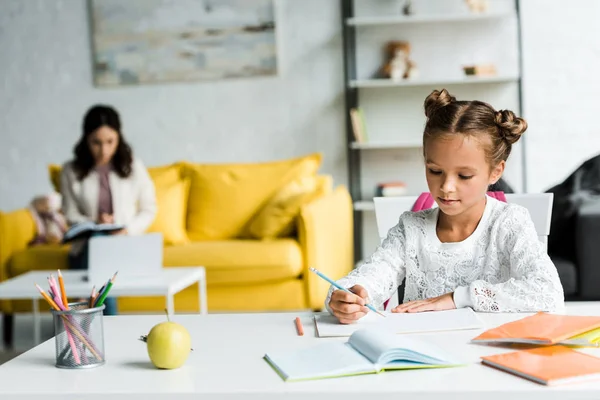 Selective focus of cute kid drawing near books and mother — Stock Photo