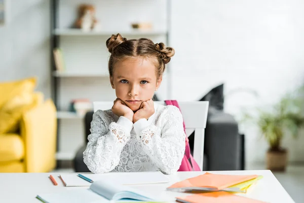 Verärgertes Schulmädchen schaut zu Hause in die Kamera neben Büchern — Stockfoto