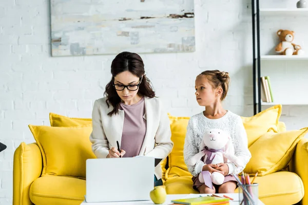 Mignon enfant tenant jouet doux et regardant la mère près de l'ordinateur portable — Photo de stock