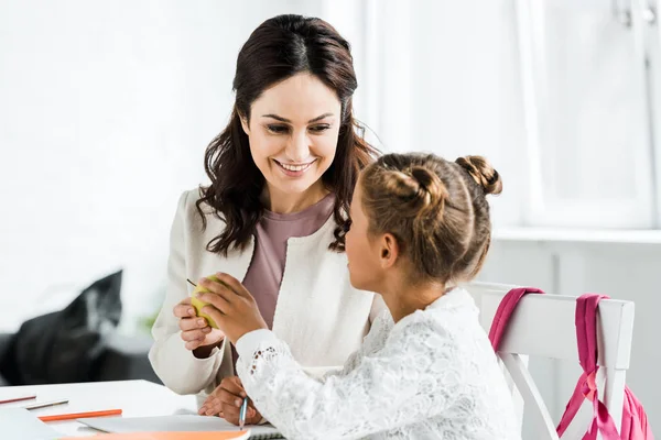 Feliz madre dando manzana a hija en casa - foto de stock