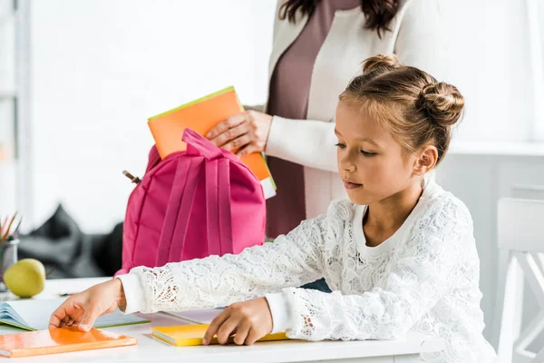 Cropped view of mother putting book in pink backpack — Stock Photo