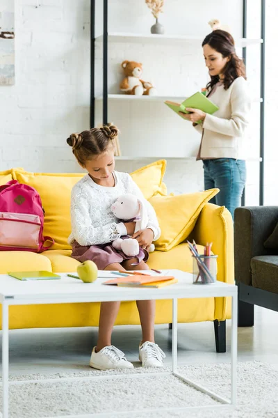 Selective focus of kid holding soft toy while sitting on sofa near mother — Stock Photo