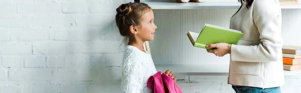 Panoramic shot of mother holding book near kid at home — Stock Photo