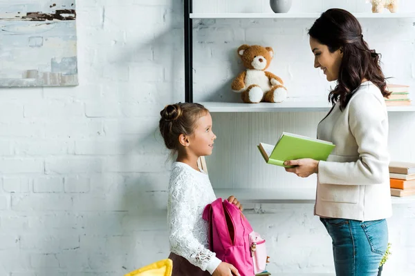 Attractive mother holding book near kid at home — Stock Photo