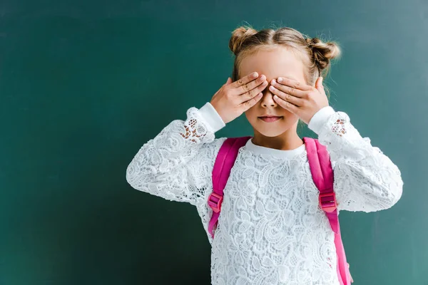 Mignon écolier couvrant les yeux avec les mains sur vert — Photo de stock
