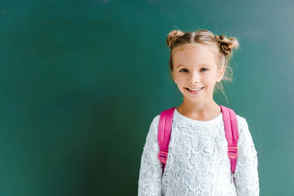 Glückliches Kind lächelt im Stehen mit Rucksack auf Grün — Stockfoto