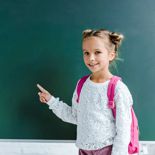 Happy kid smiling while pointing with finger at green chalkboard — Stock Photo