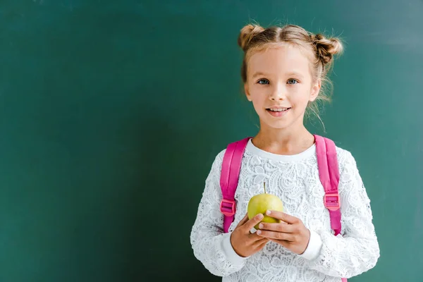 Щасливий школяр тримає яблуко на зеленому — стокове фото
