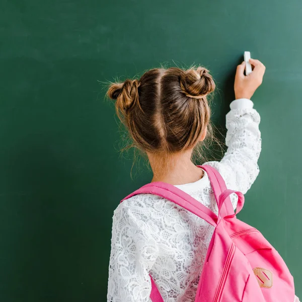 Back view of kid holding chalk near chalkboard on green — Stock Photo