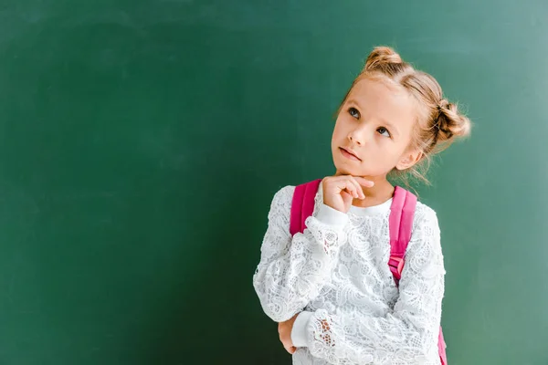 Pensive kid standing with backpack on green — Stock Photo