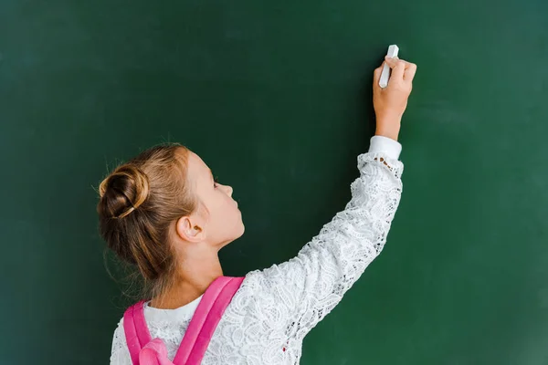 Schulkind hält Kreide neben Kreidetafel auf Grün — Stockfoto
