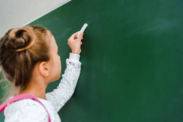 Selective focus of schoolgirl holding chalk near green chalkboard — Stock Photo