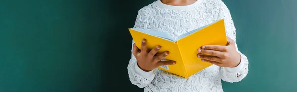 Panoramaaufnahme eines Kindes mit gelbem Buch auf grünem Hintergrund — Stockfoto