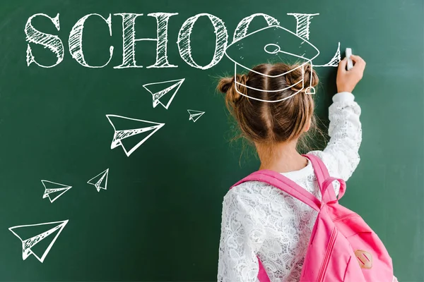 Back view of kid near green chalkboard with drawn paper planes on green — Stock Photo