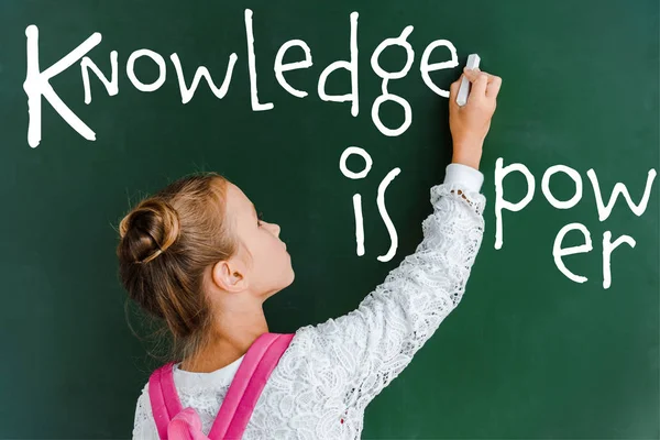Schoolchild holding chalk near chalkboard with knowledge is power lettering on green — Stock Photo