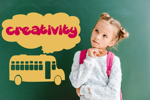 Pensive kid standing with backpack near chalkboard with school bus and creativity lettering on green — Stock Photo