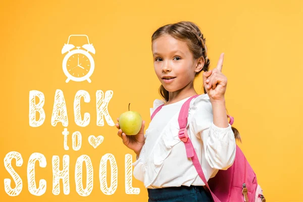 Adorable schoolkid holding apple and pointing with finger near back to school lettering on orange — Stock Photo