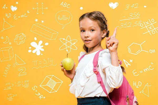 Adorable colegial sosteniendo manzana y señalando con el dedo cerca de fórmulas matemáticas en naranja - foto de stock