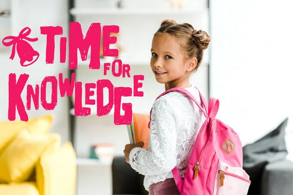 Criança da escola sorrindo que prende livros ao estar com a mochila perto do tempo para letras do conhecimento — Fotografia de Stock