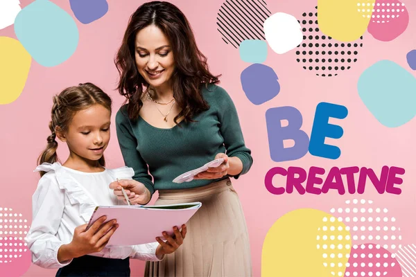 Happy mother standing near cute daughter and be creative lettering while painting on pink — Stock Photo