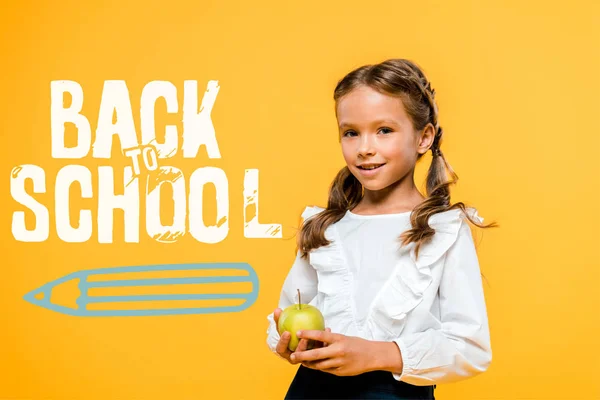 Happy schoolchild holding tasty apple near back to school lettering on orange — Stock Photo